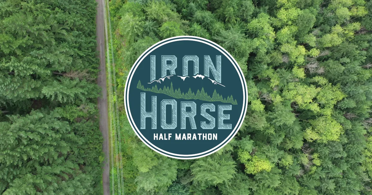 Aerial view of a road through a dense forest with the Iron Horse Half Marathon logo in the center.