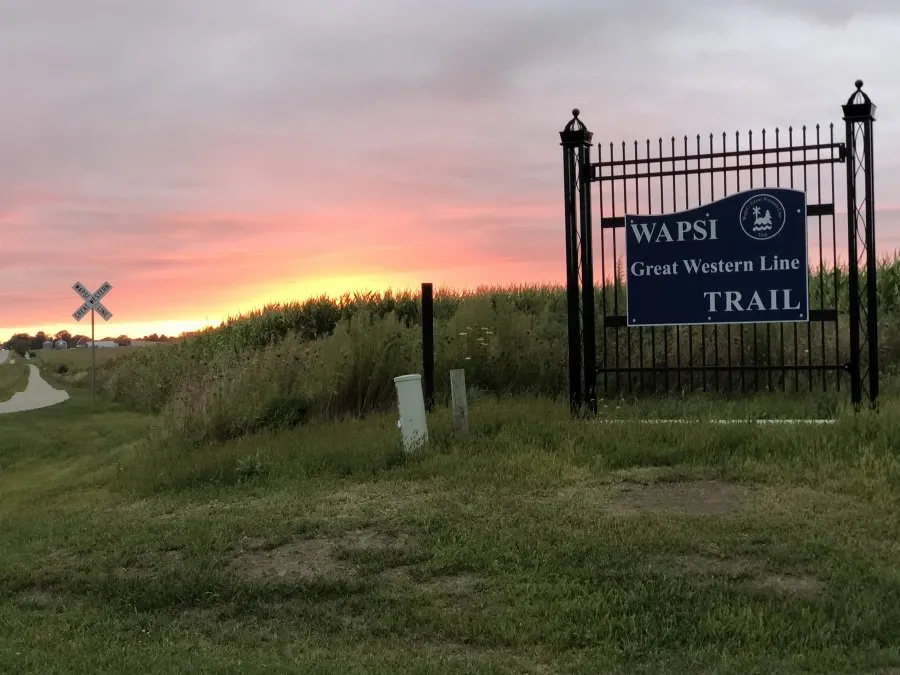 The entrance to the Wapsi Great Western Line Trail with a sign and a railroad crossing sign at sunset.