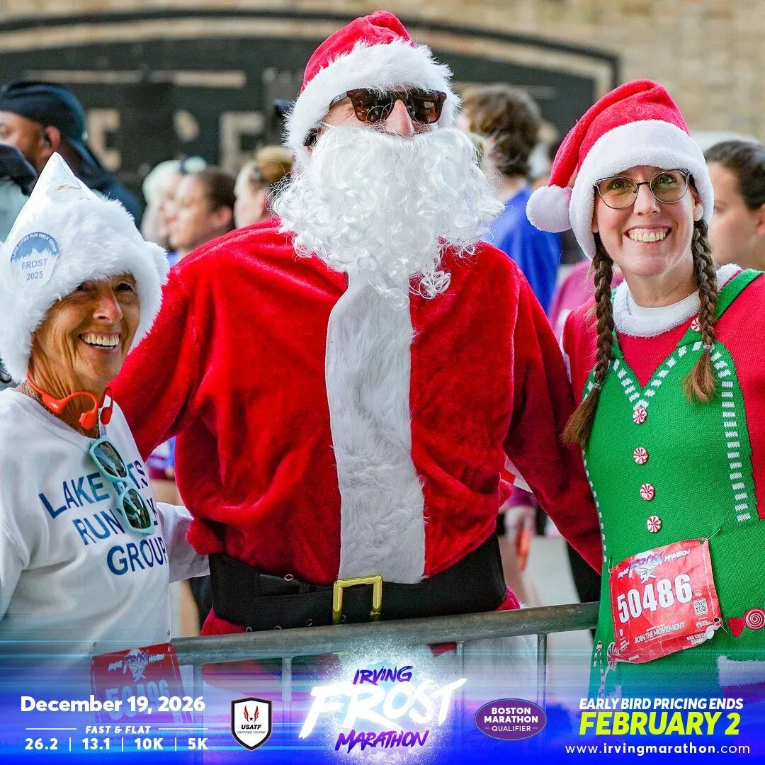 Three people in festive Santa and elf costumes smiling at the camera, with race bibs visible, suggesting a fun and celebratory atmosphere at the Irving Frost Marathon.