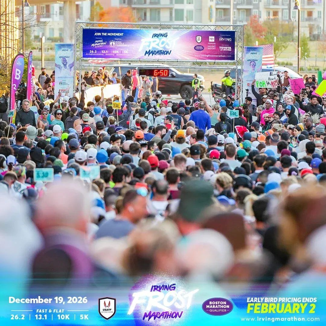 A large crowd of runners gathered at the start line of the Irving Frost Marathon, with a banner overhead and a digital clock showing the time.