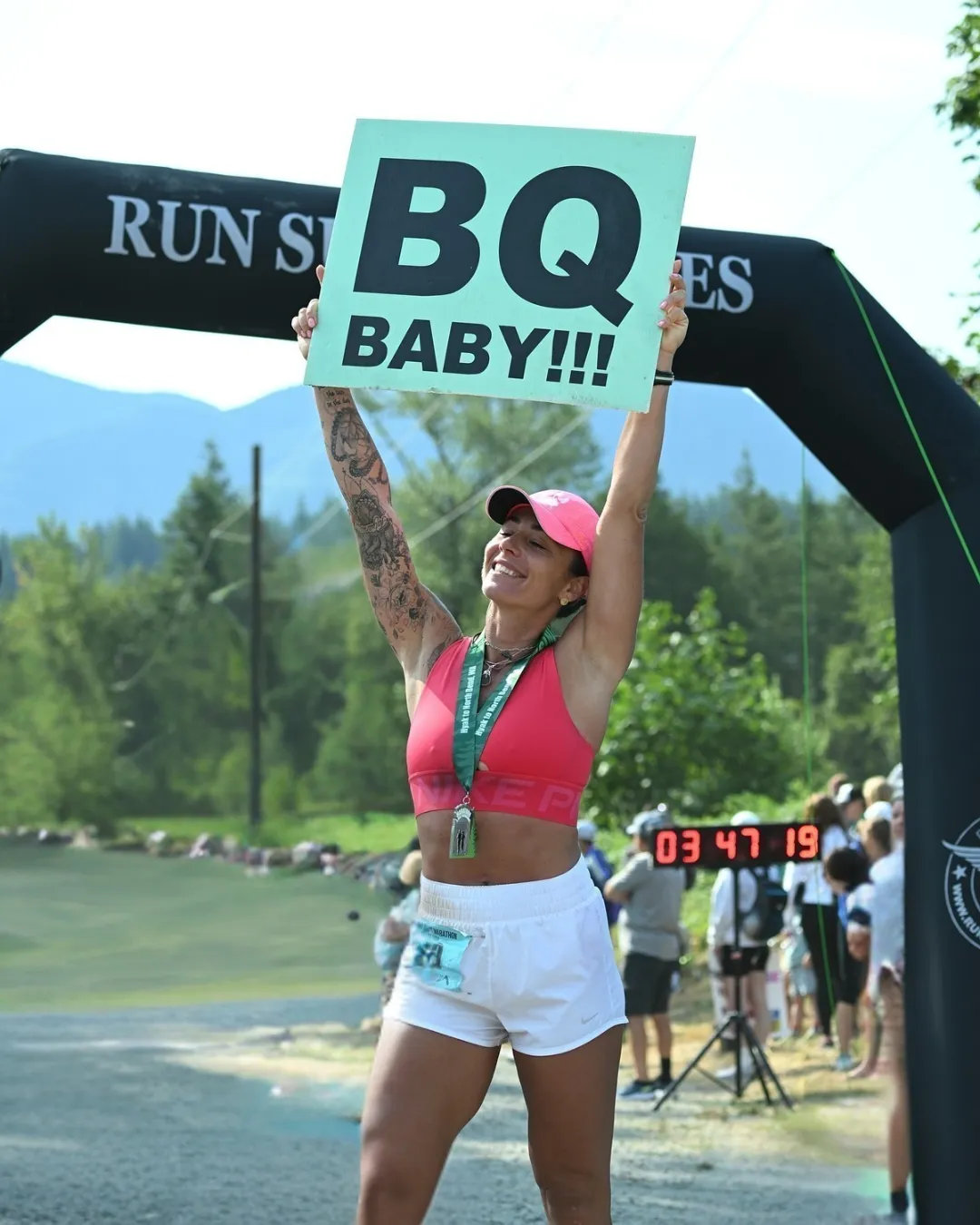 A runner celebrates achieving a Boston Qualifier at the Jack and Jill Marathon, holding up a sign that says 'BQ BABY!!!' and wearing a medal.