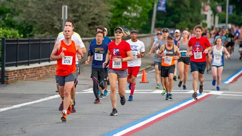 Runners in a race, with bib numbers visible, running on a road with red, white, and blue lane markers.