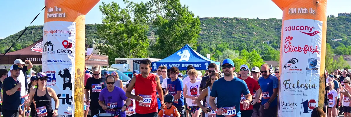 Runners gathered at the start line under an inflatable archway, with a scenic mountain backdrop.