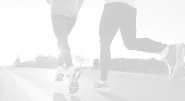 Two runners seen from the knees down, running on a road with the sun in the background.