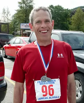 A smiling male runner wearing a red shirt, a medal, and a bib with the number 96.
