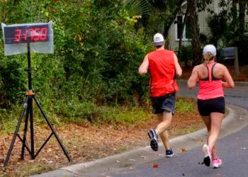 Two runners on a road course, with a digital clock displaying 3:47:50.