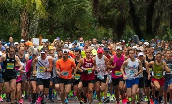 A large group of runners starting a marathon, with palm trees in the background.