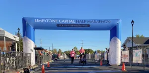 Runners crossing the start/finish line under a blue inflatable archway for the Limestone Capital Half Marathon.