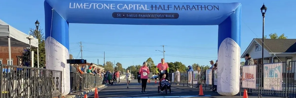 Runners crossing the start/finish line under a blue inflatable archway at the Limestone Capital Half Marathon.