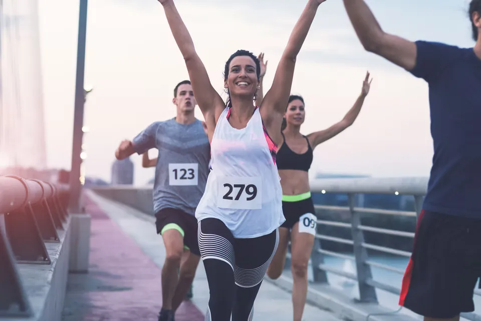 Runners with arms raised in celebration crossing the finish line on a bridge.