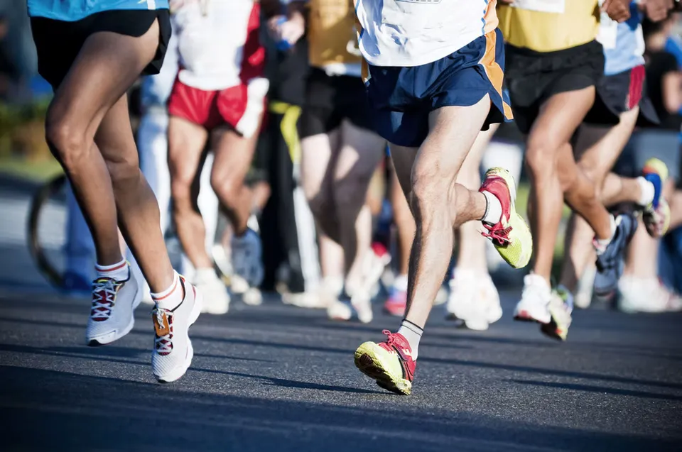 Close-up of runners' legs and feet as they race on a road, with a shallow depth of field.