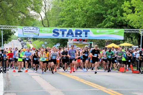 A large group of runners starting the Lola's Half Marathon, with a banner overhead that reads 'START'.
