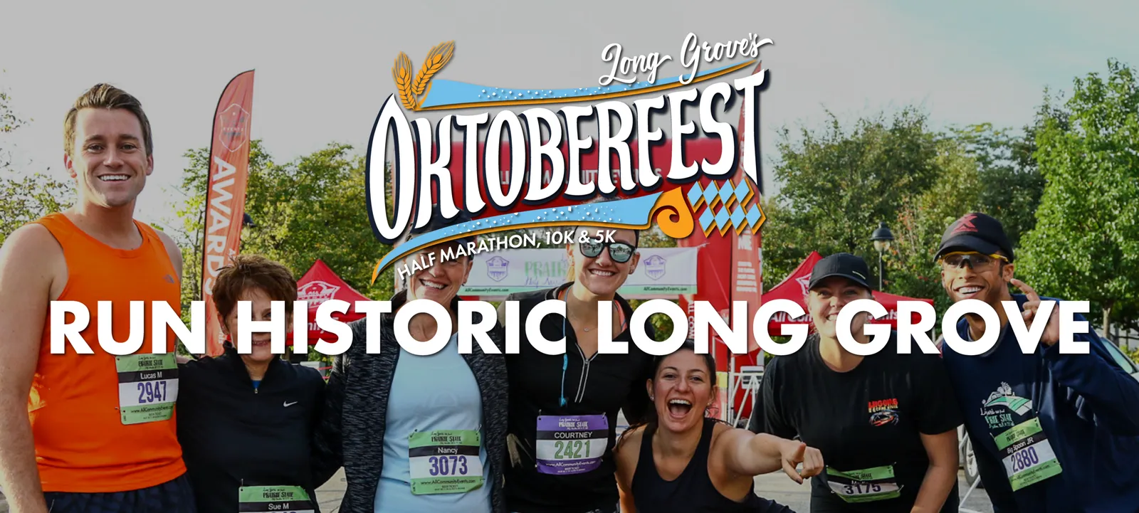 A group of happy runners posing for a photo at the start line of the Long Grove Oktoberfest Half Marathon, 10K & 5K, with the race logo prominently displayed.