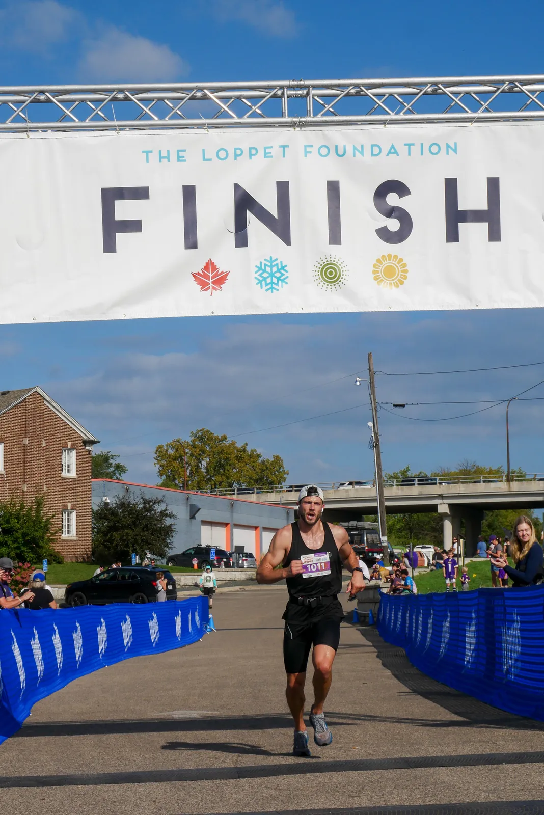 A male runner with bib number 1011 crosses the finish line under a banner that reads "THE LOPPET FOUNDATION FINISH".