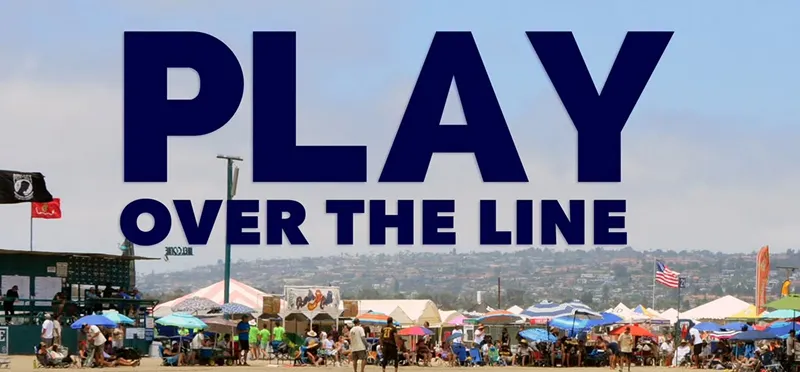 A large crowd gathers on a beach with tents and umbrellas, under a sky with the words "PLAY OVER THE LINE" in large blue letters.