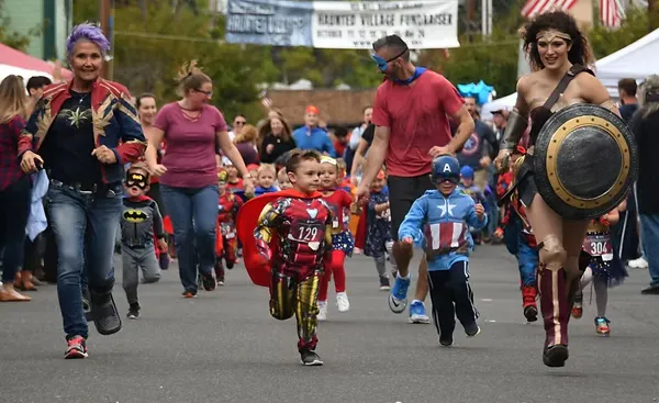 Children and adults dressed as superheroes, including Iron Man, Captain America, Batman, and Wonder Woman, run in a race.