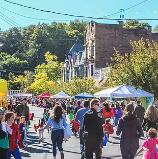 A street scene with many people, tents, and buildings, suggesting a race expo or start line event.