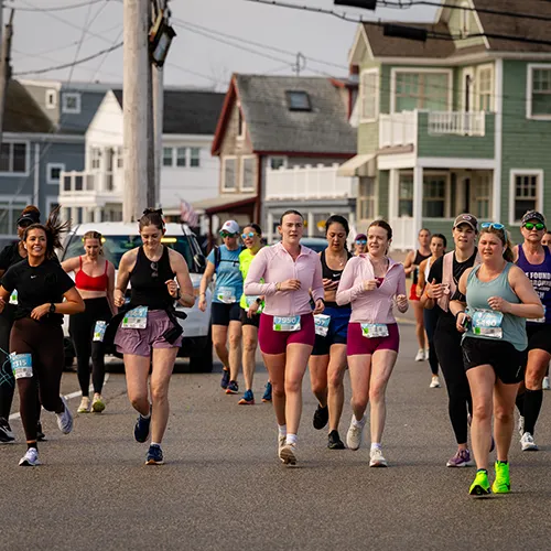 A group of female runners are running down a street lined with houses.