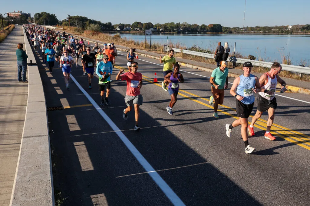 Runners race across a bridge with a waterfront view.