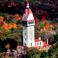 A tower with a red roof stands on a rocky outcrop surrounded by trees displaying vibrant autumn colors.