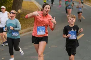 A woman in an orange shirt and a young boy in a black shirt run a race, with the woman making a fun gesture.