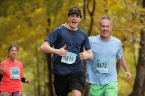 Two male runners give thumbs up while running, with a female runner in the background.