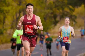 A male runner with bib number 366 smiles and gives a thumbs up while running on a road, with other runners behind him.