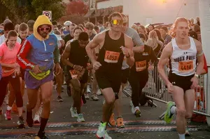 Runners starting a race, with several in the foreground and a crowd in the background.