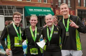 Four runners wearing medals and race shirts smile for the camera after completing the Mankato Marathon Half Marathon.