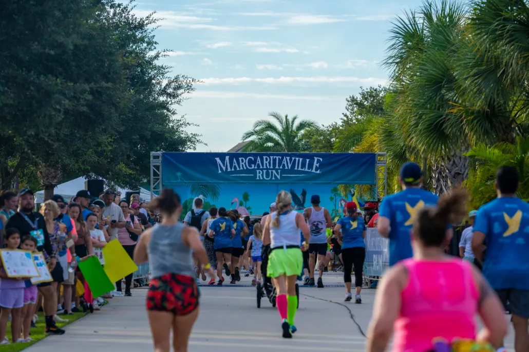 Runners crossing the start line under the Margaritaville Run banner, with spectators cheering on the side.
