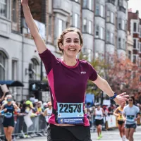 A female runner with her arm raised in celebration, wearing bib number 22579, crosses the finish line of a road race.