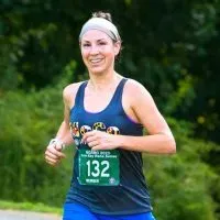 A female runner with a headband smiles as she runs, wearing a bib with the number 132.