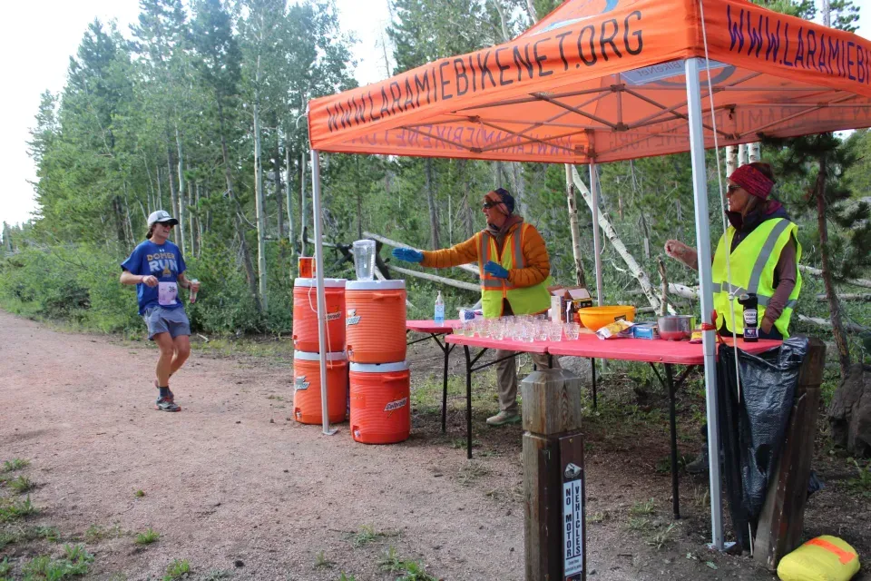 A runner approaches an aid station with volunteers handing out drinks.