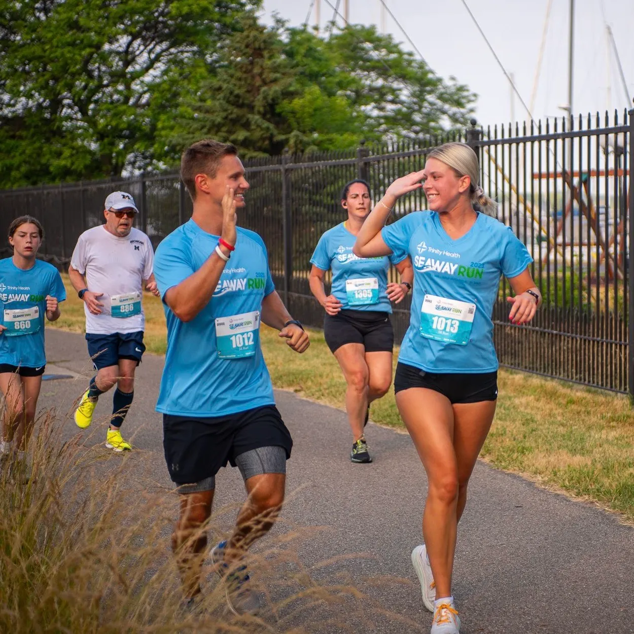 Runners in blue 'Seaway Run' t-shirts high-fiving each other while running on a paved path.