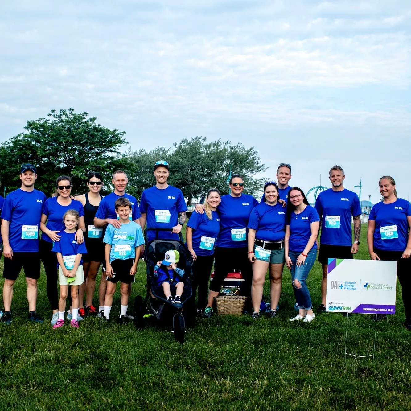 A group of runners in blue shirts pose for a photo on a grassy field, with a stroller in the foreground.