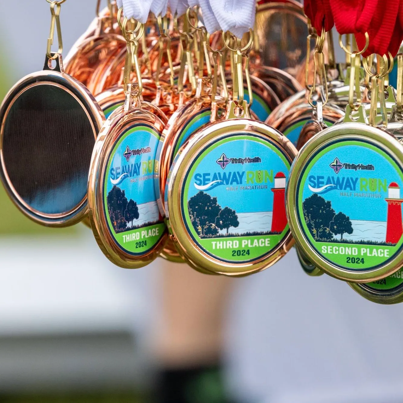 A collection of Seaway Run Half Marathon medals for third and second place in 2024, featuring a lighthouse and trees.