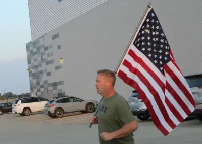 A man in a green t-shirt carries an American flag while walking.
