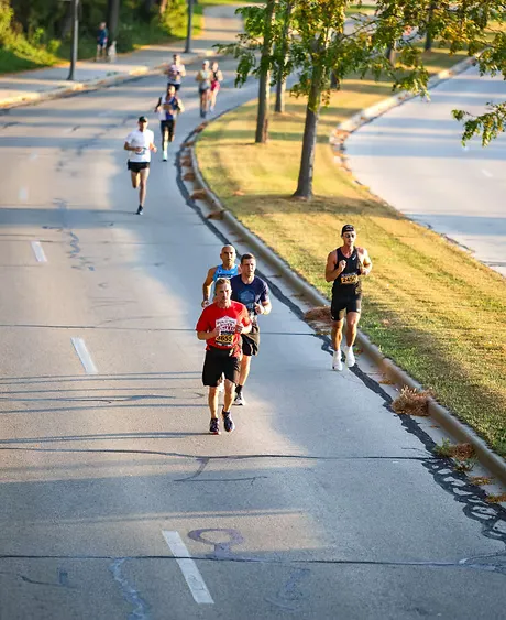 Runners on a paved road with trees lining the side.