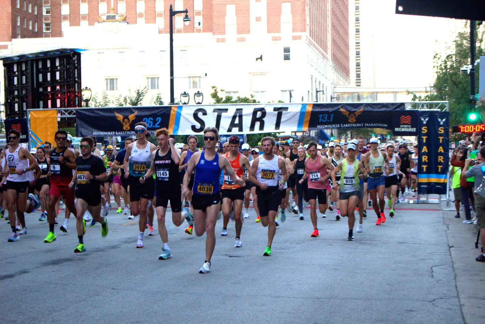 Runners starting the Milwaukee Lakefront Marathon with a banner overhead that reads 'START'.