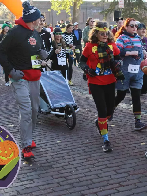 Runners in Halloween costumes, including Wonder Woman and skeleton outfits, participating in a race on a brick road.