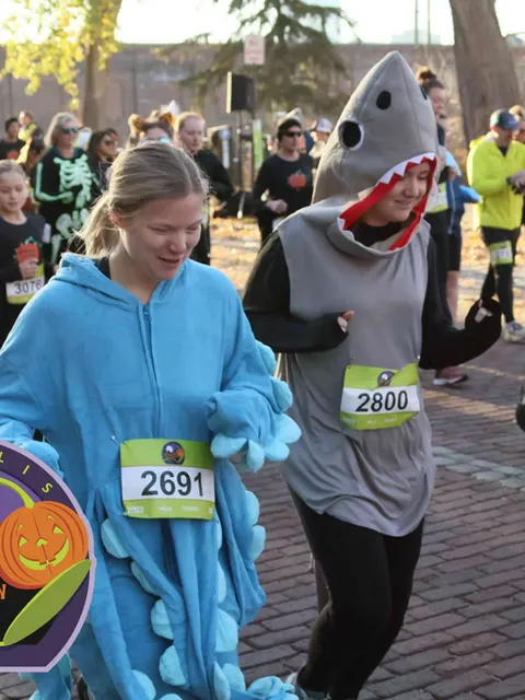 Two runners in Halloween costumes, one a blue monster and the other a shark, participating in a race.