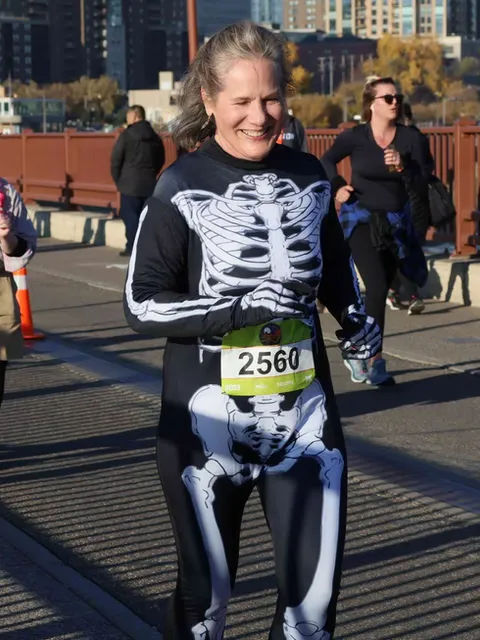 A woman in a skeleton costume smiles while running in a race.