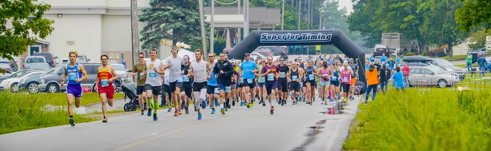 A large group of runners starting a race under a 'Superior Timing' archway.