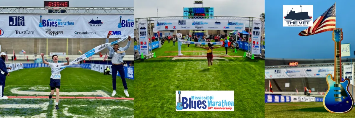 Runners celebrating as they cross the finish line at the Mississippi Blues Marathon, with a large guitar statue and American flag in the background.