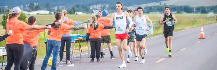 Runners receiving drinks from volunteers at an aid station during a road race.
