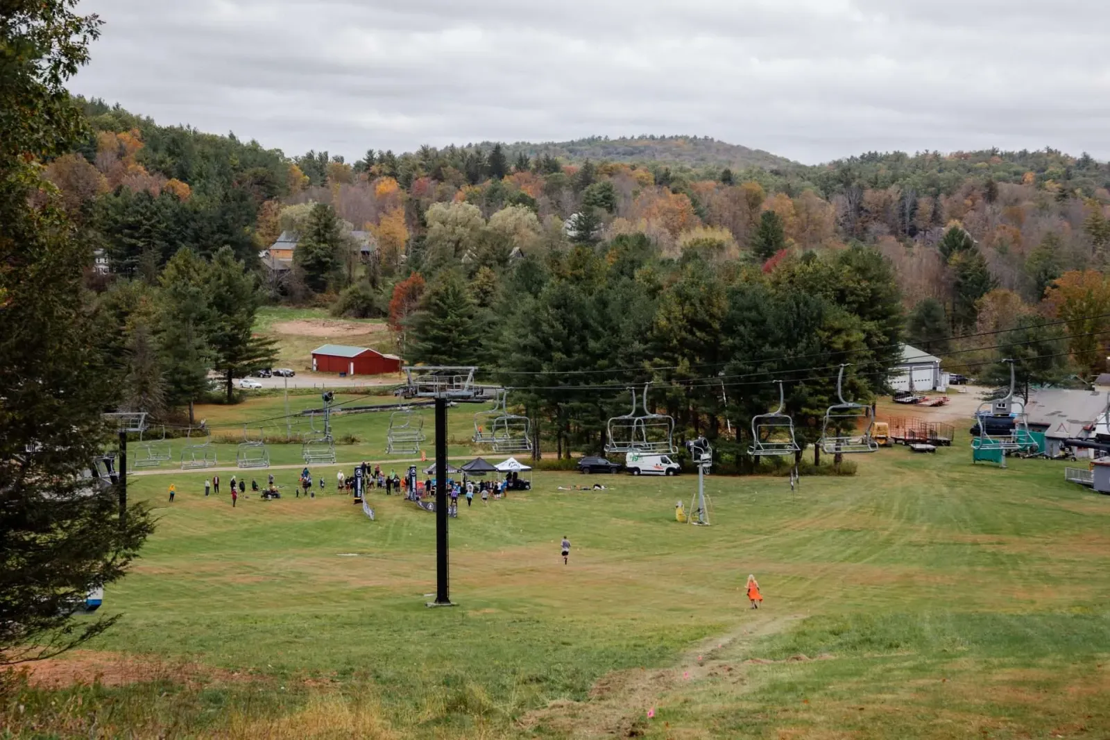 Runners gather near tents and ski lifts at the base of a mountain, with autumn foliage visible on the surrounding hills.