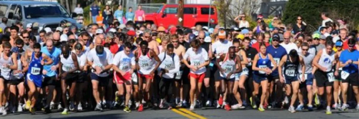 A large group of runners are lined up at the start of a road race, with many of them in motion.