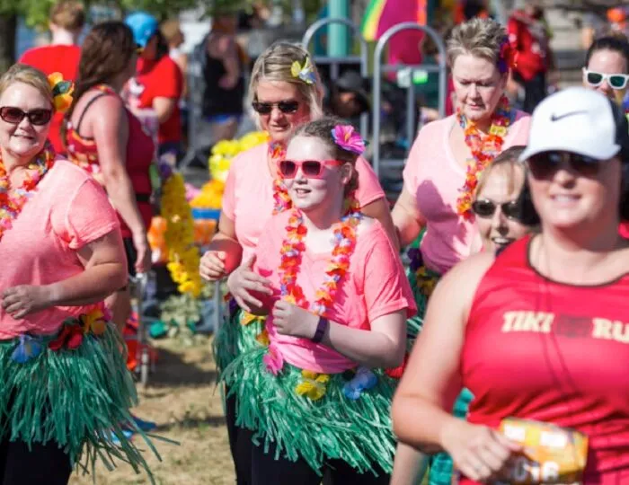 A group of women in pink shirts and grass skirts, wearing leis and sunglasses, participate in a fun run.