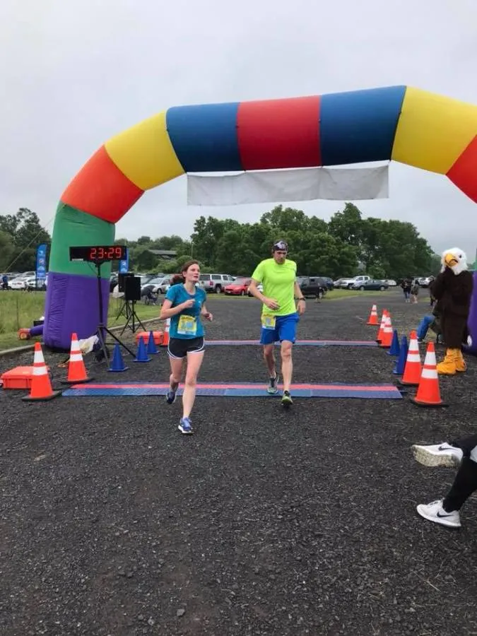Two runners, a woman and a man, crossing the finish line under a colorful inflatable archway.