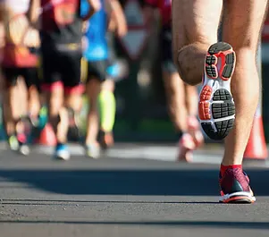 Close-up of a runner's shoe and leg as they run on a road, with other runners blurred in the background.